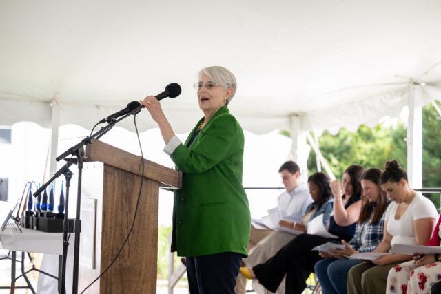 Woman with gray hair 和 in a green suit st和ing at a podium